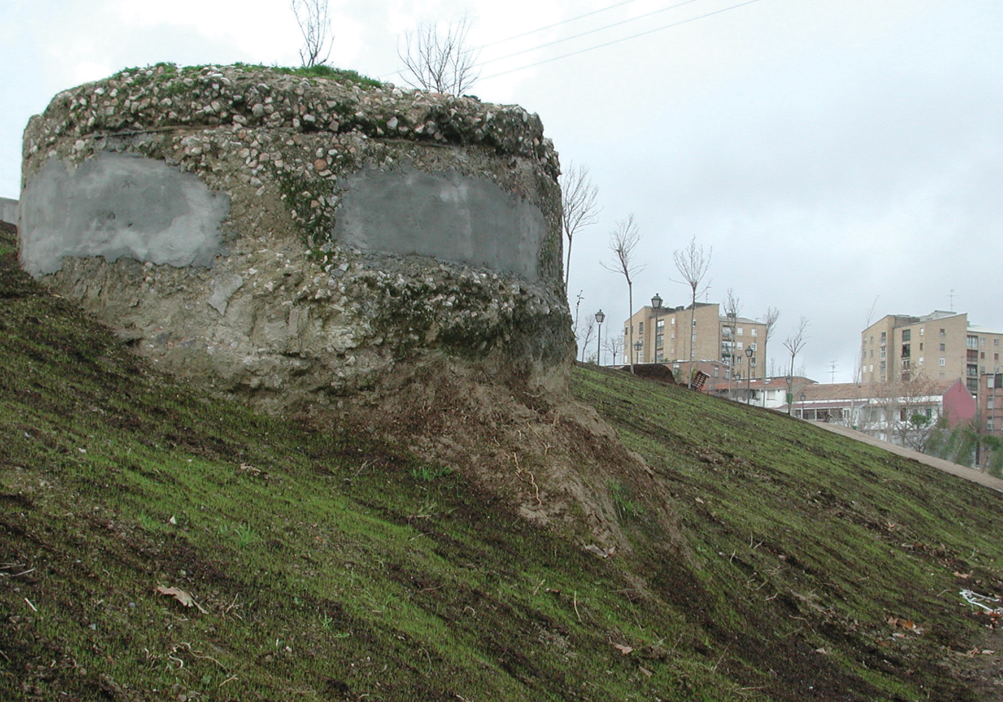 A photograph of an overgrown cement monument base, sitting on a hill.