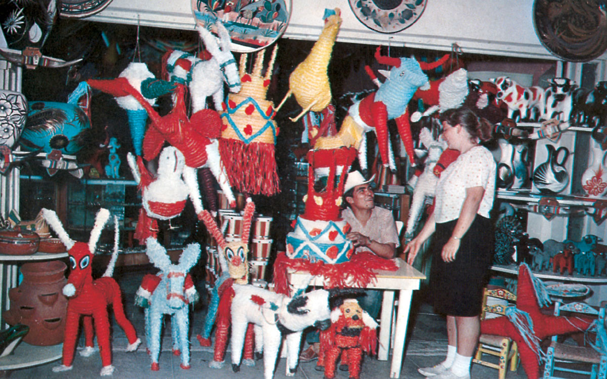 A photograph of a tourist in a Tijuana trinket shop filled with colorful straw animals. 
