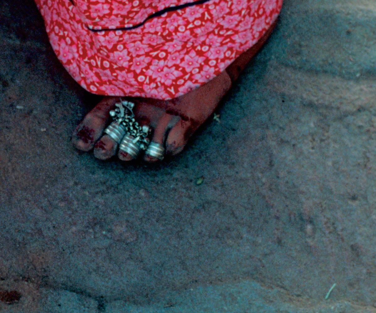 A photograph of a Jaipur foot decorated with rings and nail polish, and a bright pink floral textile on top of the foot.