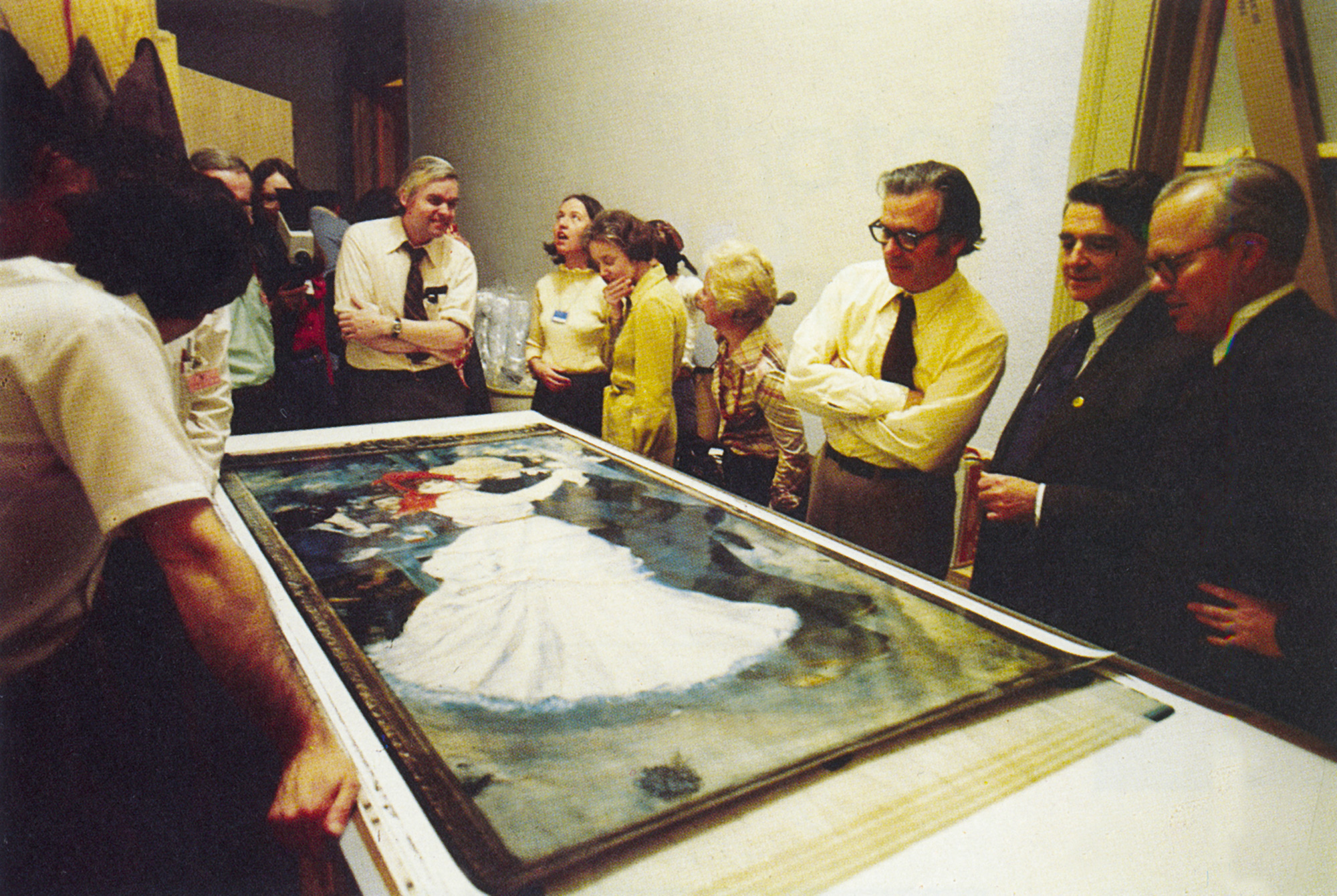 A nineteen seventy-six photograph of a group of people examining a full-size photograph of a Renoir painting at the Museum of Fine Arts, Boston. This was the first photographic replica of an artwork made using Polaroid’s room-sized “Camera Camera.”