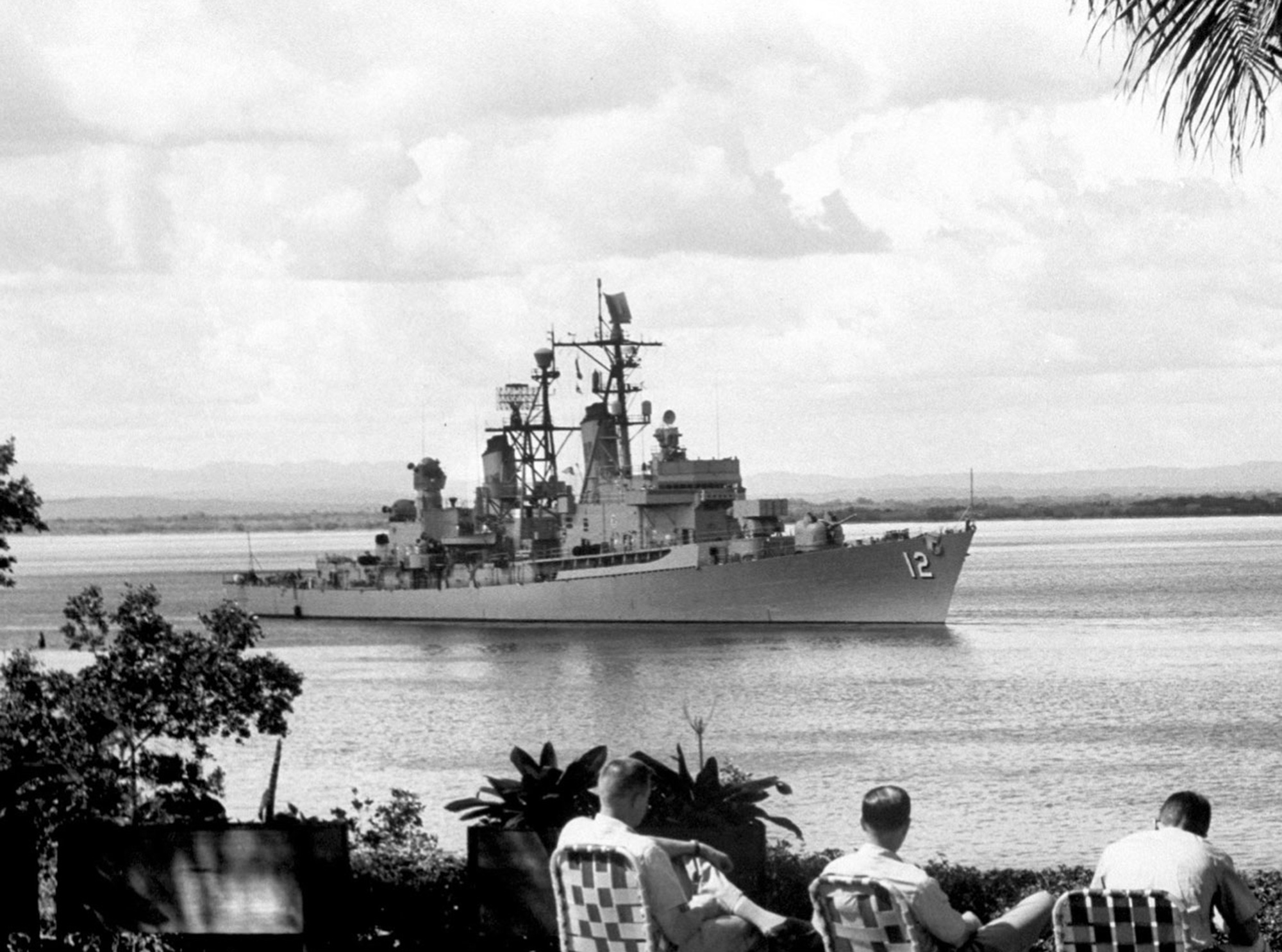 A nineteen sixty-two photograph of men sitting on deck chairs in Guantánamo Bay, looking out at the United States Armed Forces Destroyer “Sullivan,” at the time of the Cuban Missile Crisis.