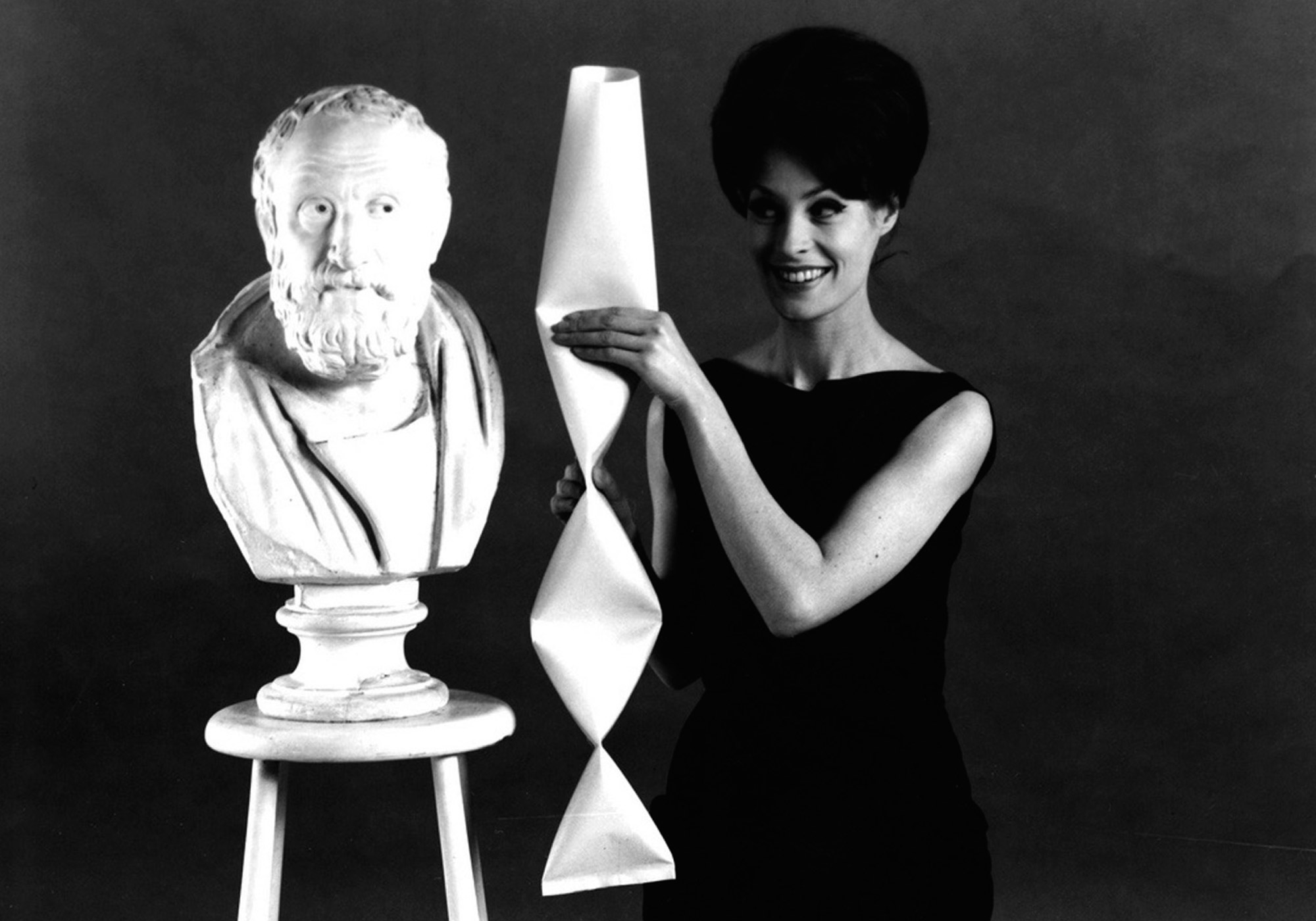 A nineteen sixties promotional image for Tetra Pak, featuring a woman holding a rhombic columnal assemblage of Tetra Pak packets next to a bust of Plato.