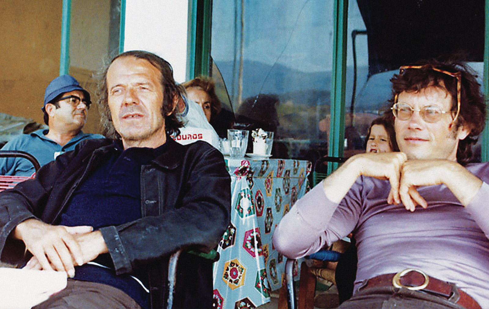 A circa nineteen eighty photograph of Gilles Deleuze and Félix Guattari sitting at a table on the Greek island of Skyros.