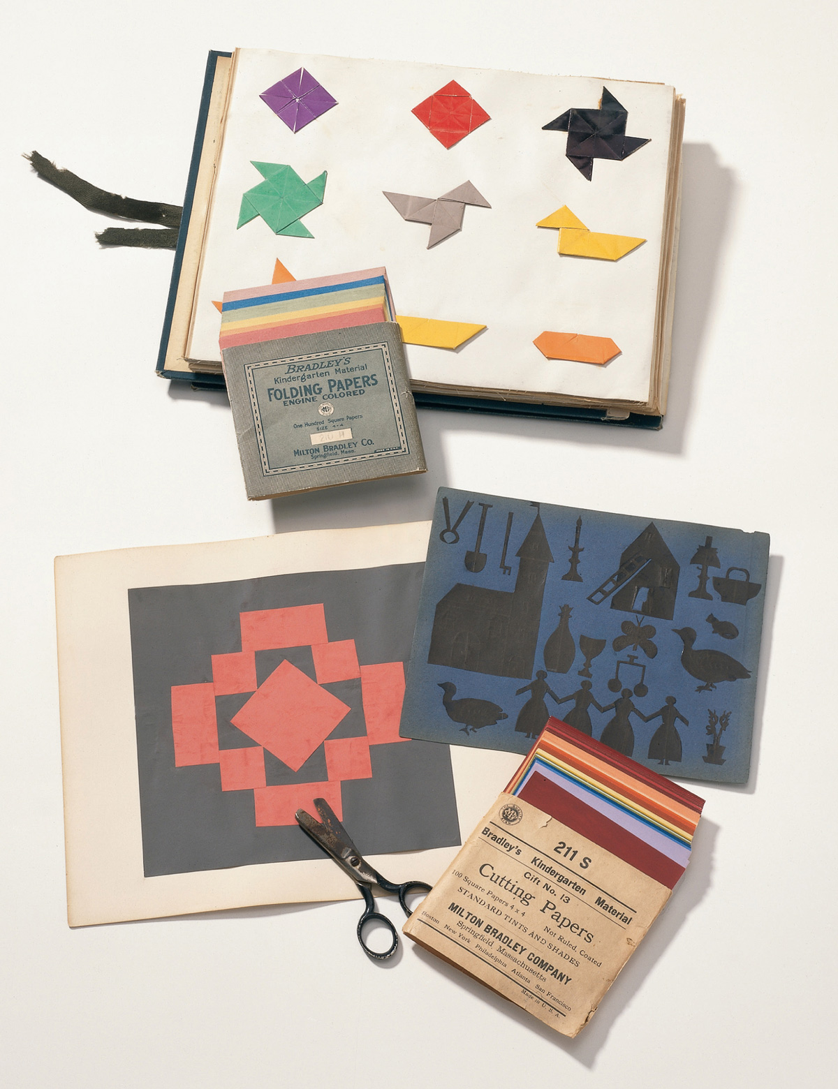 A photograph of various materials related to Friedrich Wilhelm Fröbel‘s pedagogical system. These include kindergartners’ and teachers‘ exercises made by folding and cutting paper.