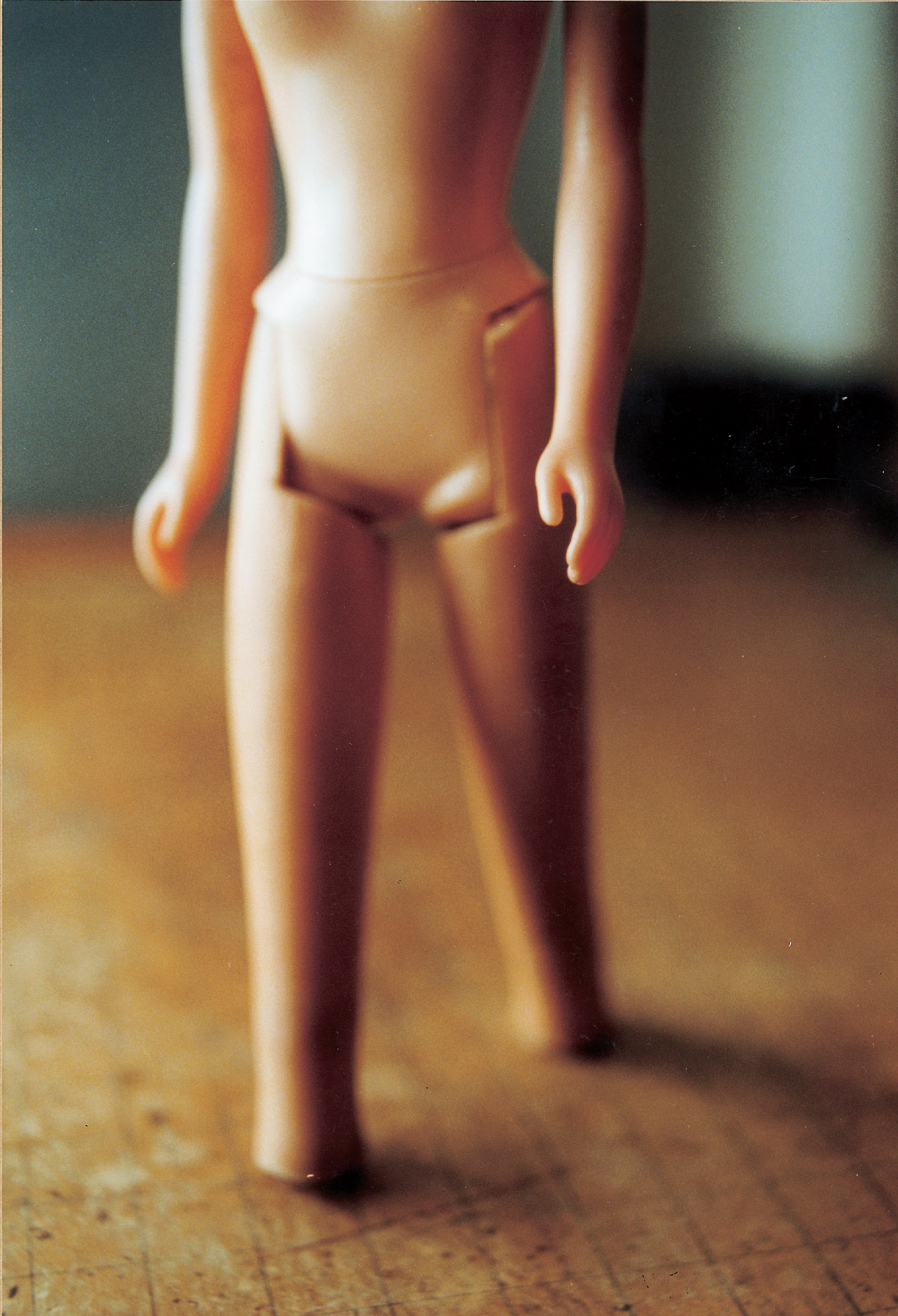 A photograph depicting a detail view of an unclothed doll named Barbie. The caption reads: Long snubbed by the Doll Games, a “found” Barbie was finally admitted in the late classical period, on the condition that she suffer her trademark blonde hair to be dyed black, and her legs to be amputated just below the knees. Unfortunately, the offensive “blackface” and ungainly leg stumps that resulted from these operations made her a laughingstock, and she never found a lasting place in the Doll Games; her name, if she was given one, has been forgotten.