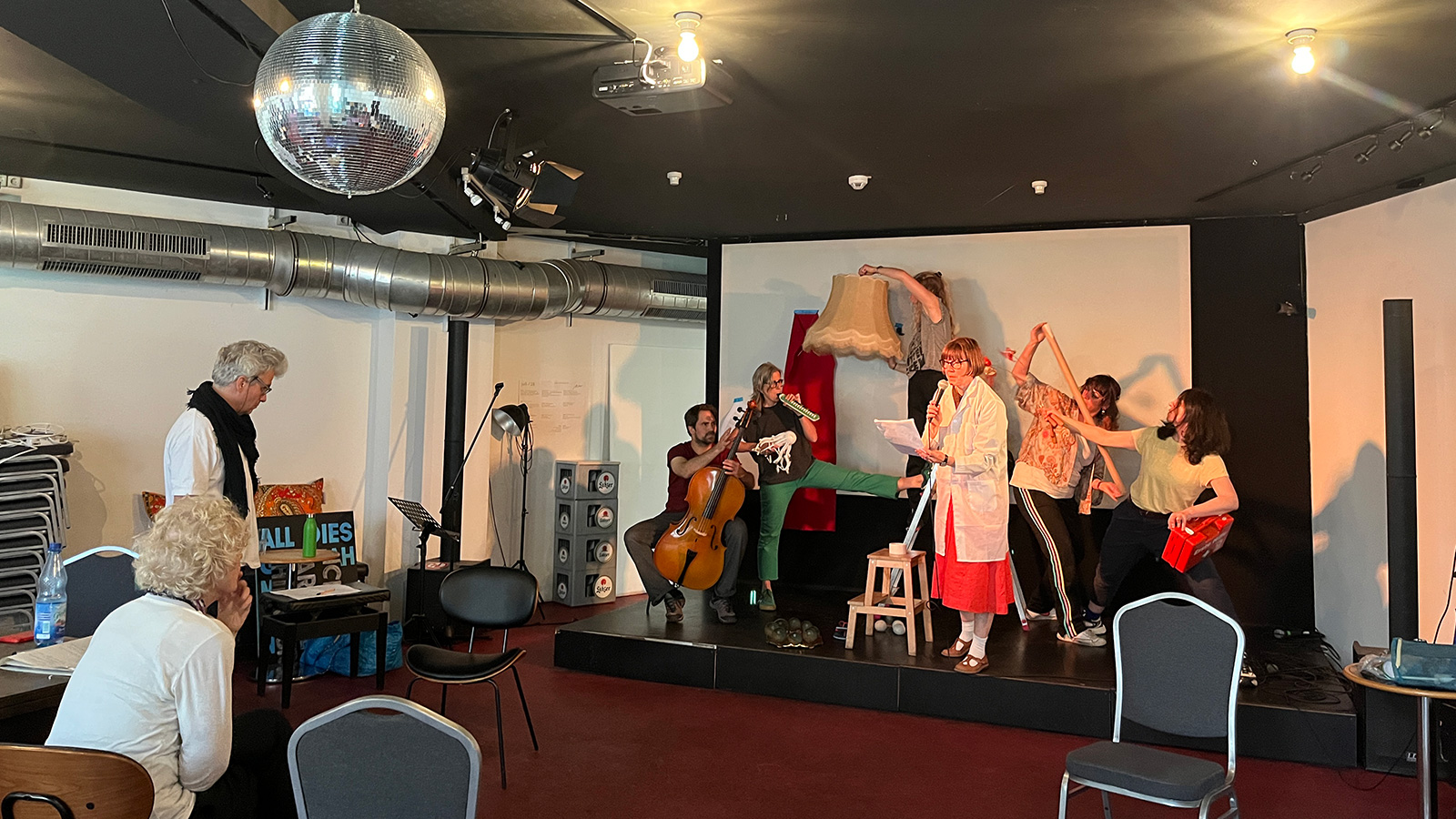 A photograph taken during rehearsals of the performers creating a text-to-voice conversion machine using their bodies as well as various musical instruments and objects.