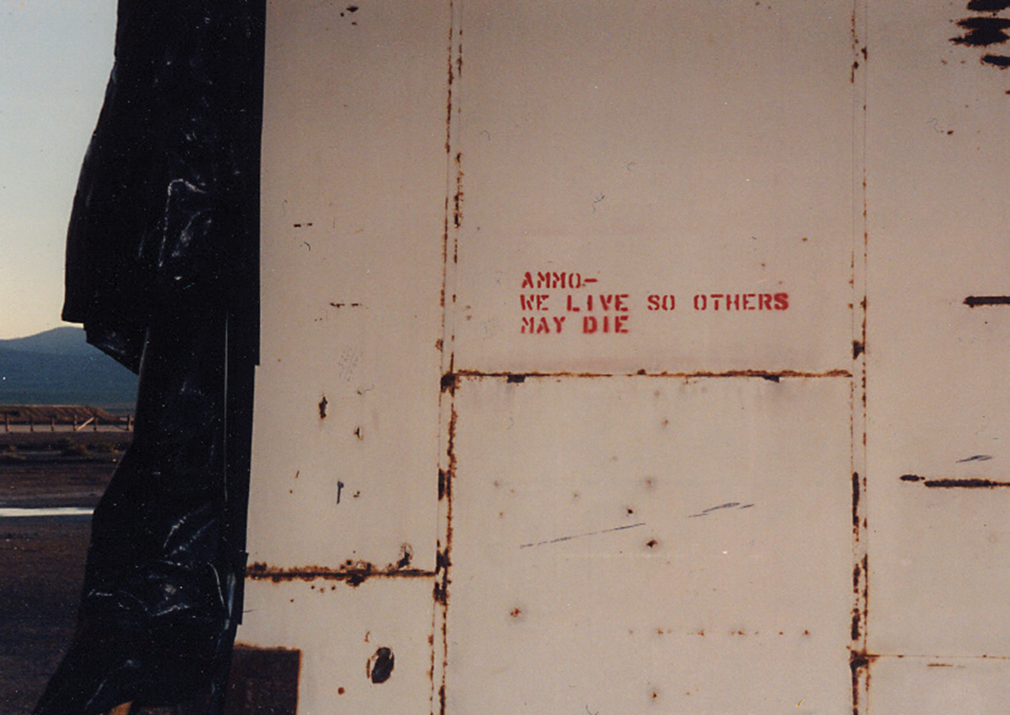 A photograph of the phrase “Ammo-we live so that others may die” stenciled on a structure.