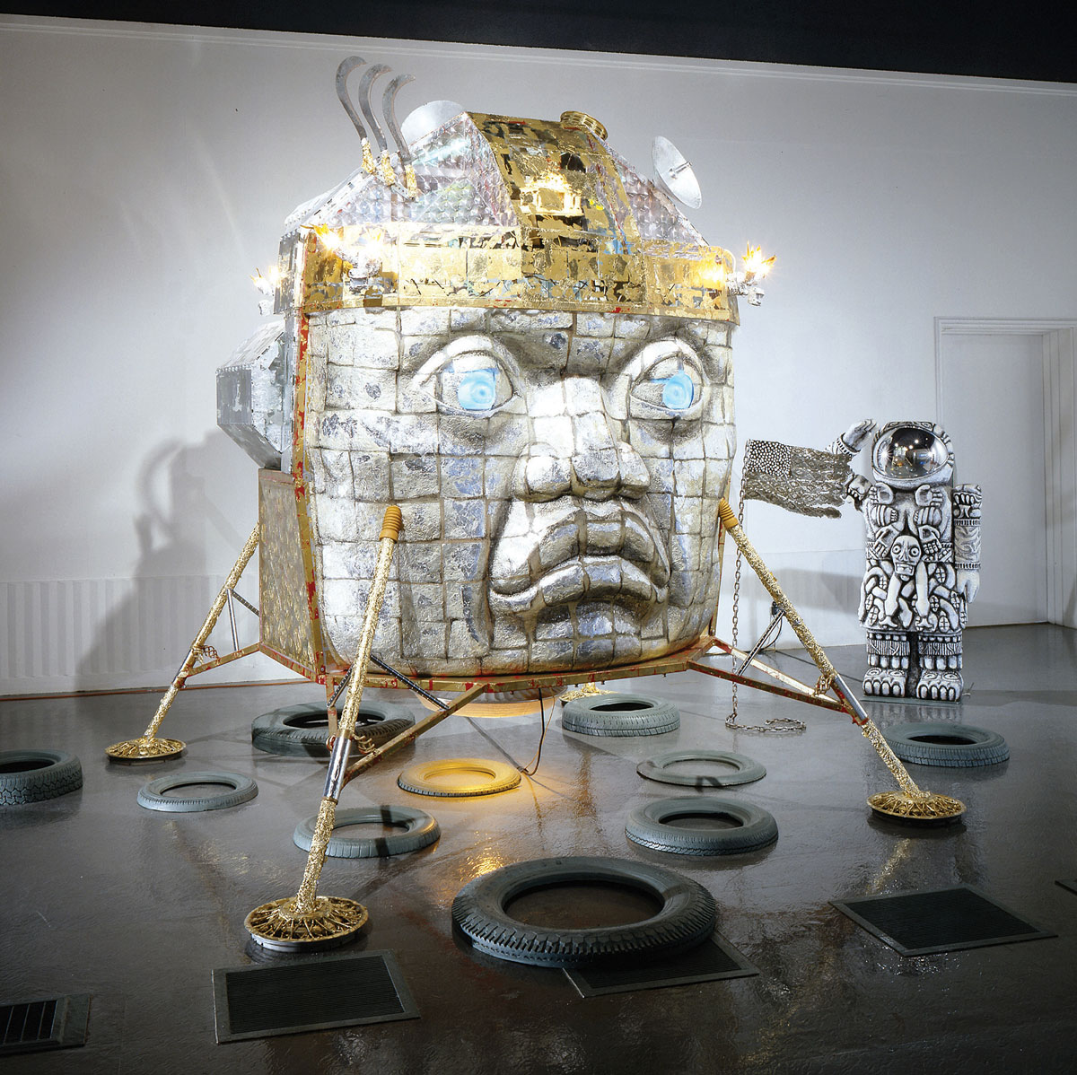 A photograph of a 2002 mixed media installation of a large metallic head by Einar & Jamex de la Torre, entitled “Colonial Atmosphere.”