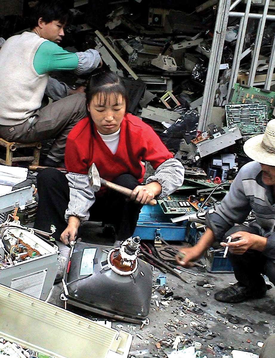 A photograph of a Chinese woman using a hammer to smash a computer monitor while wearing no protective equipment.