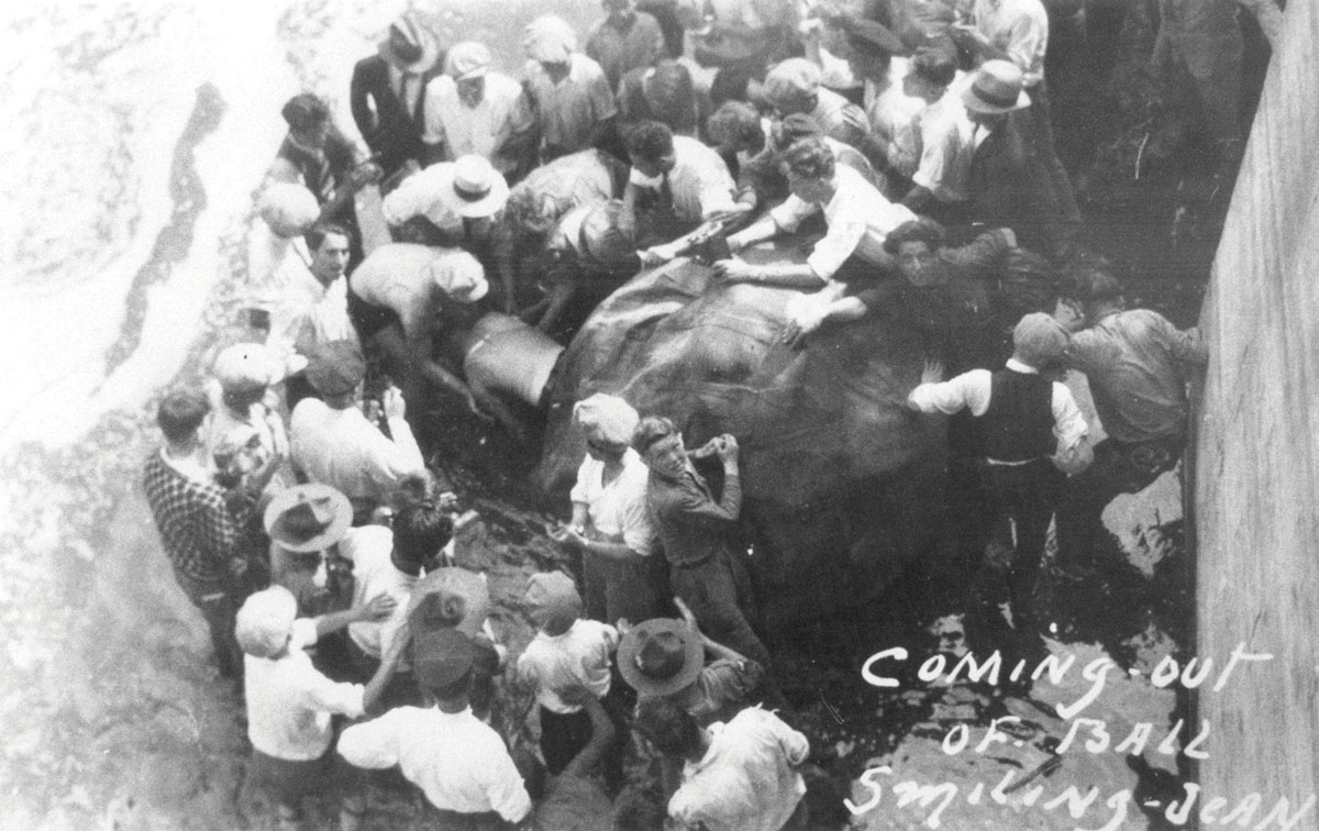 A photograph of a crowd surrounding Jean Lussier, who is emerging from the rubber ball in which he had just rolled over the falls on the 4th of July 1928.