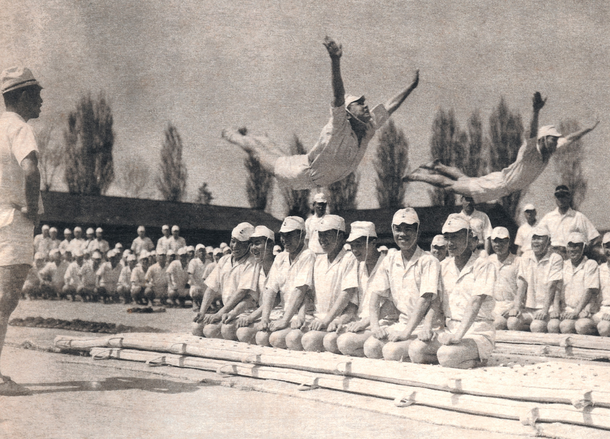 A photograph showing men in uniform leaping through the air with their arms outstretched, a basic mat exercise for the students in the Primary Aviation Course.