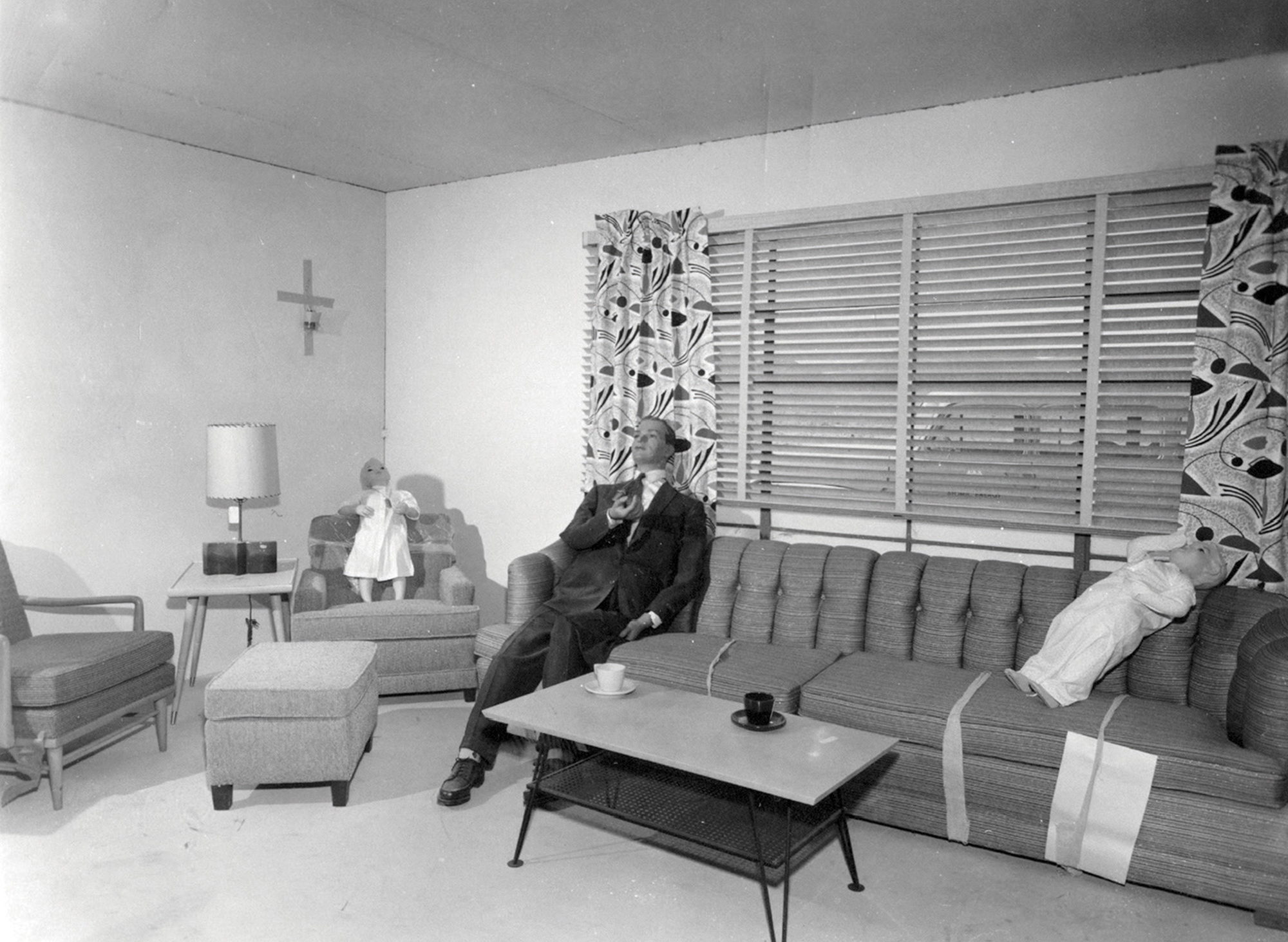 A photograph from Operation Cue depicting a male test dummy sitting on a couch in a living room.