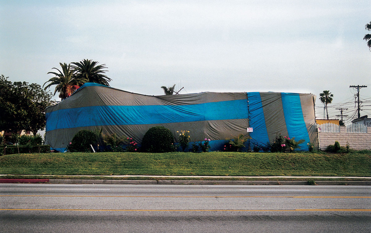 Artist Susan Silton’s photograph of a house enveloped in striped tarpaulin.
