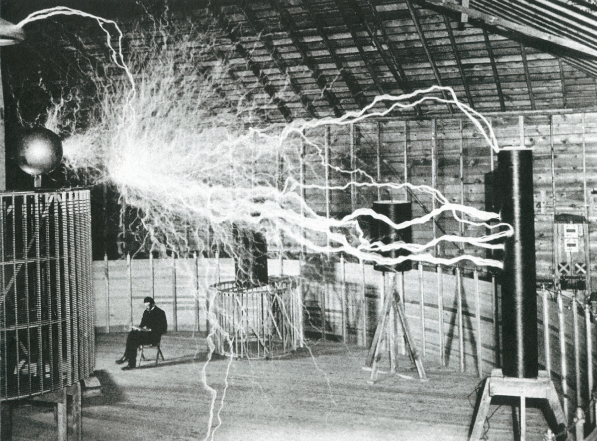 A photograph of Nikola Tesla at his laboratory in Colorado Springs, peacefully reading as millions of volts from his Magnifying Transmitter crackle overhead. In his notes, Tesla identified the photo, which was taken around nineteen hundred, as a double exposure produced for publicity purposes.