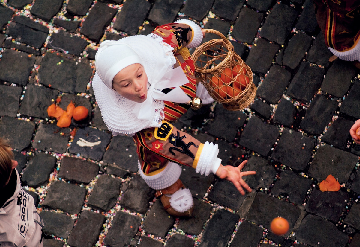 A two thousand four photograph of a child tossing an orange in the air at the Carnival in Binche, Belgium.