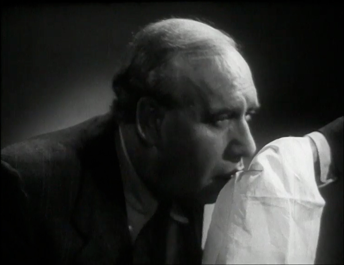 A film still from “Handkerchief Drill,” nineteen forty nine, directed by Michael Orrom. A demonstrator induces a sneezing fit in actor Richard Massingham by showering him in pepper to show the correct use of a handkerchief. This one-minute public information film made by the British COI (Central Office of Information) reminded cinema audiences that “coughs and sneezes spread diseases.” 