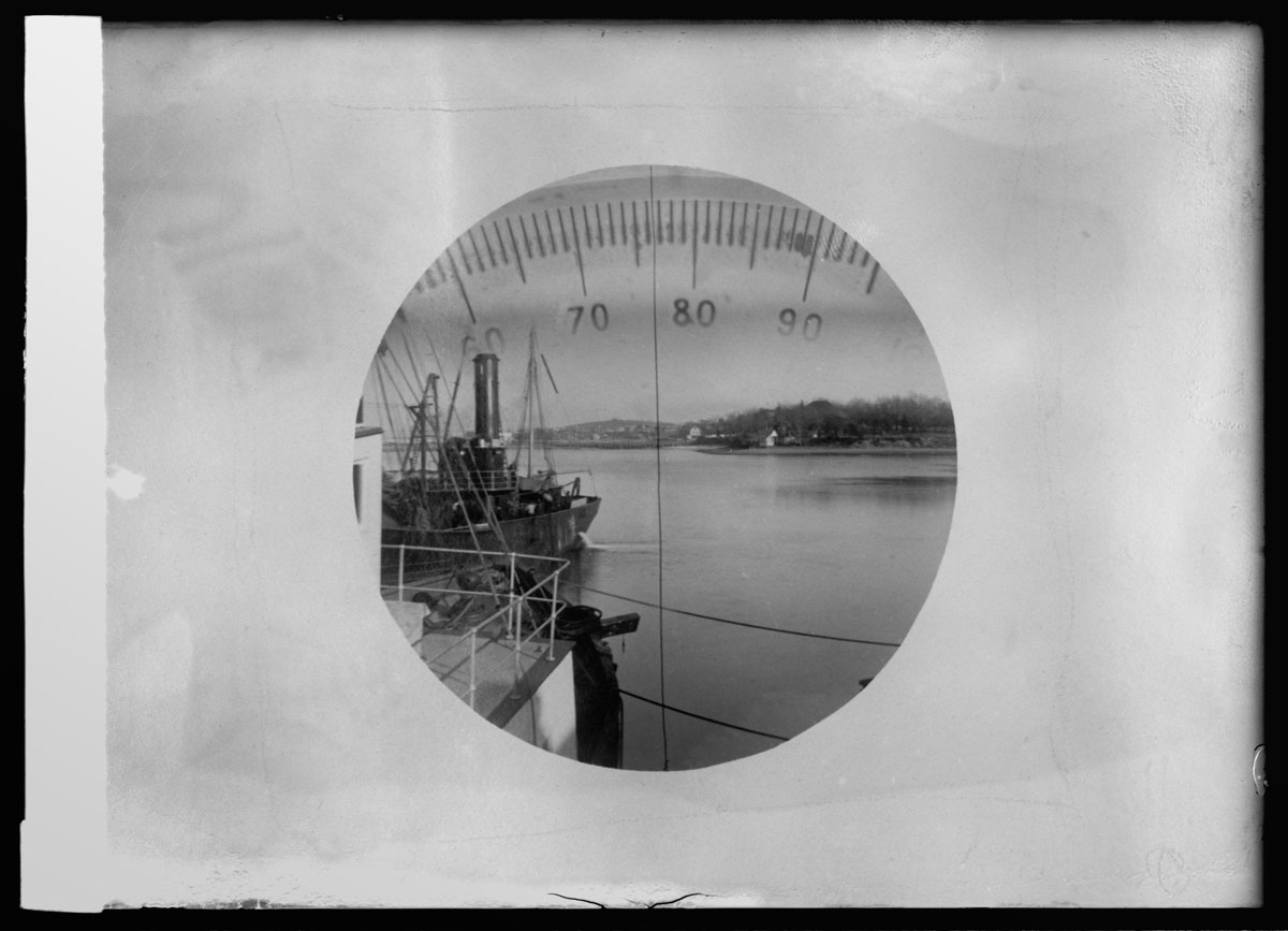 A photograph, taken between between nineteen oh eight and nineteen nineteen, of the view of a ship at sea through a submarine’s periscope. 