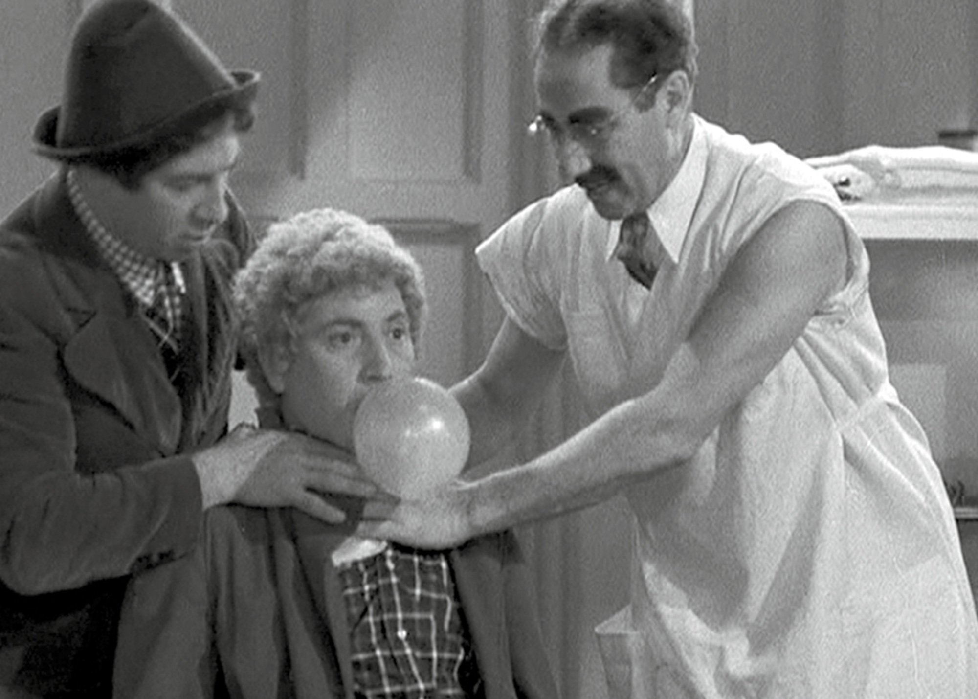 A still from the nineteen thirty-seven film “A Day at the Races” depicting Harpo Marx blowing a bubble with chewing gum.