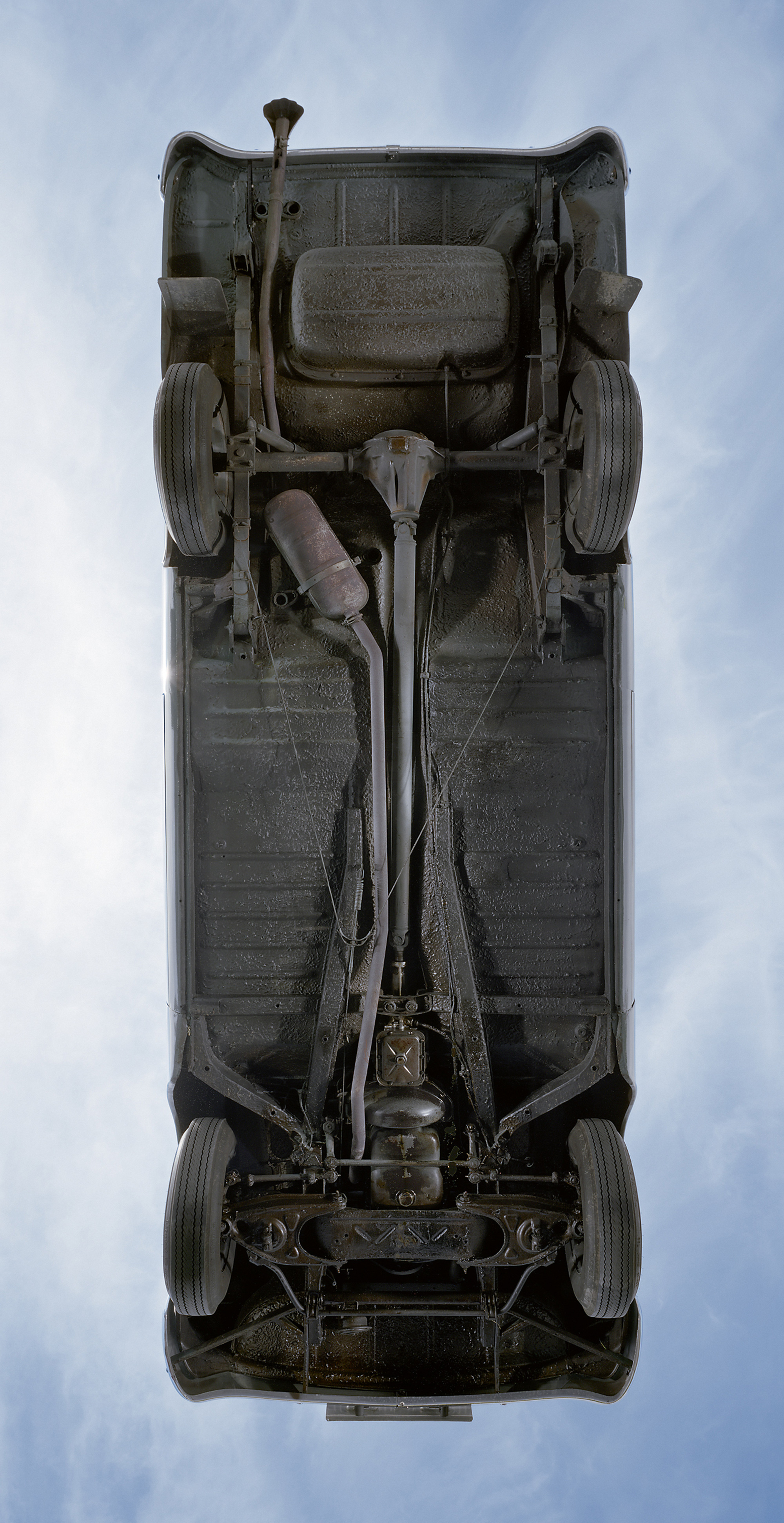 A photograph of the underbelly of a car resting on a large sheet of heavy-duty glass. 