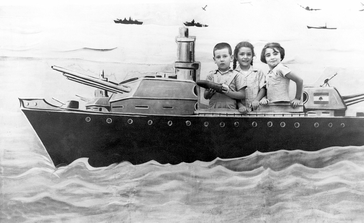 A photograph taken in 1955 in Zahleh, Lebanon, of three children—Farid Najjar, Chadia Najjar, and Nina Chahinian—posing behind a cutout of a military ship.