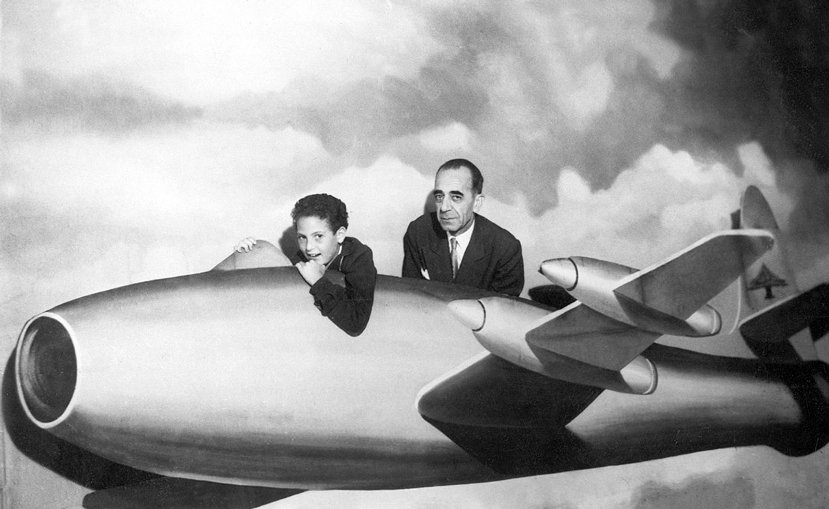 A photograph taken in 1958 in Zahleh, Lebanon, of Antoine Sehnaoui and his son and Nebil posing behind a cutout of an airplane.