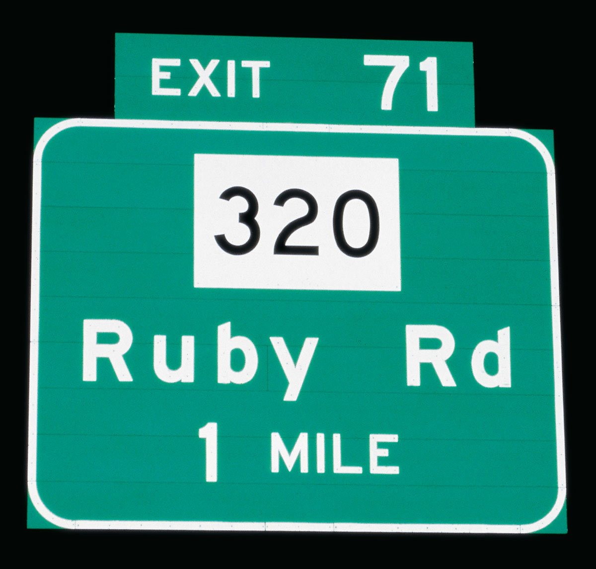 A photograph of a highway exit sign for Ruby Road, exit 71, taken at night.