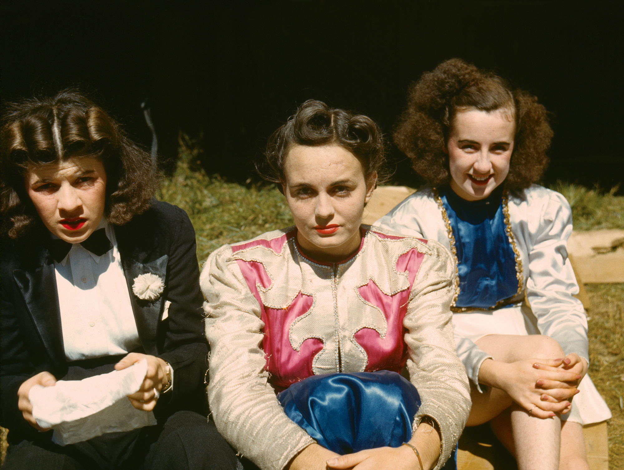 A photograph of three seated women. One wears black tie, the other two, charmeuse. 