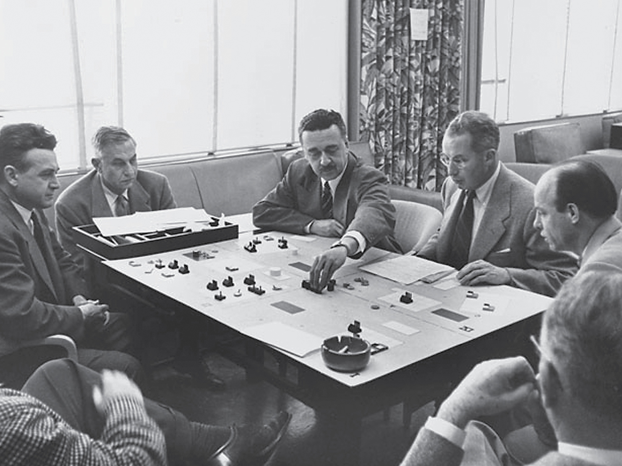 A circa nineteen fifty-four photograph of Strategic Air War Game being played at the RAND Corporation headquarters in Santa Monica, California. In the image—used by the think-tank to promote their contributions to game theory—Phil Morse, an original RAND board member, is seen making his move.
