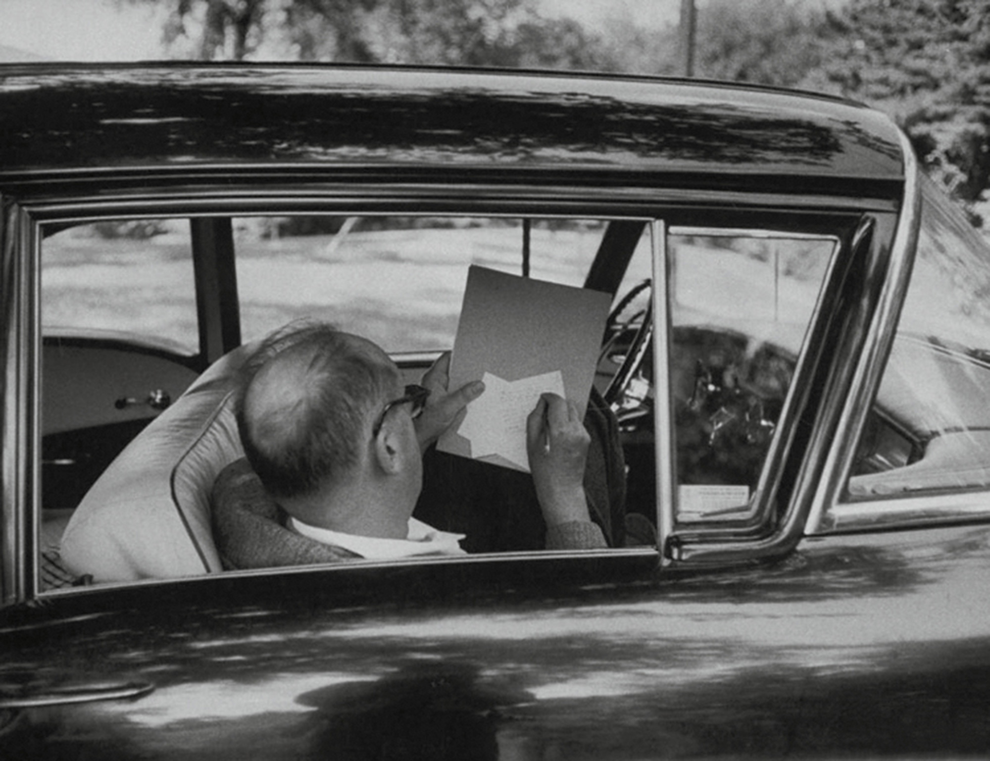 A photograph of Vladimir Nabokov scribbling on note cards in a car.