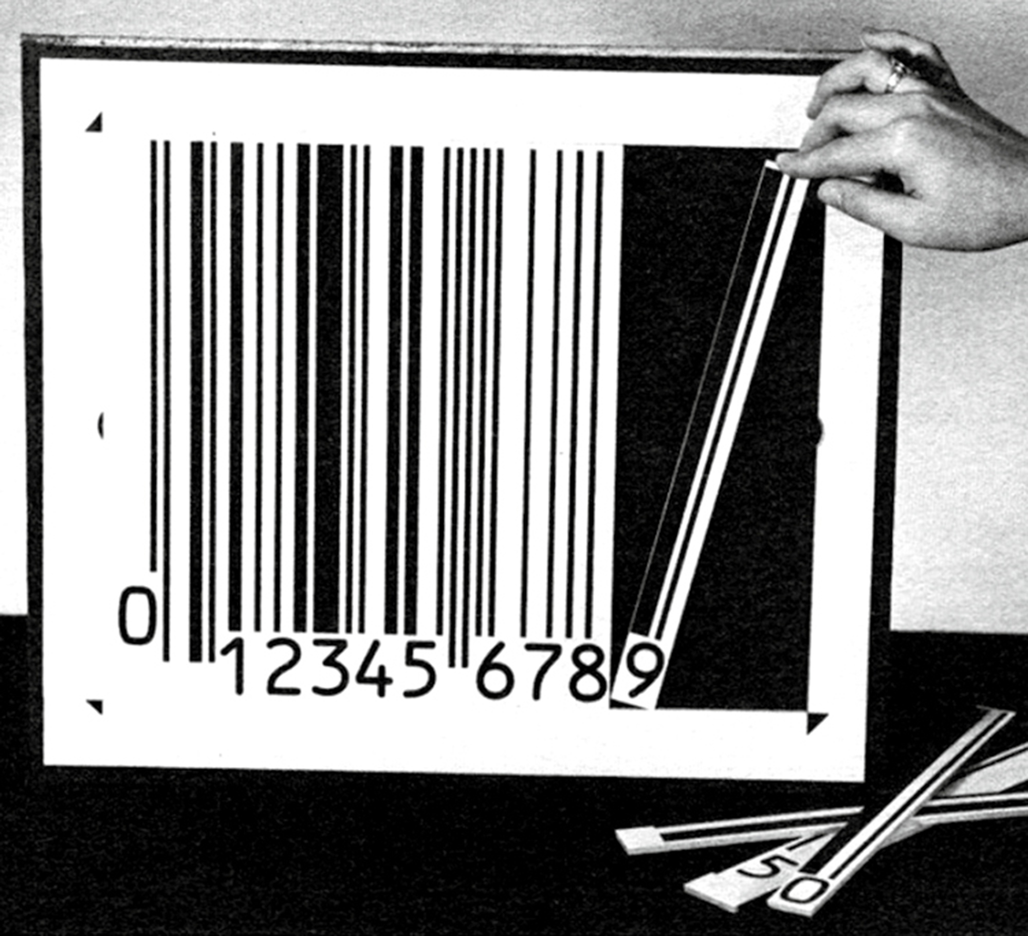 A circa nineteen seventy-three photograph of a hand doing final preparations for a photoshoot of a sample Universal Product Code.