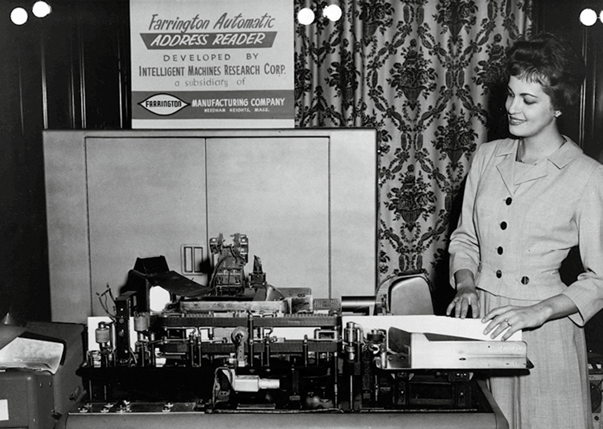 “A nineteen fifty-three photograph of a woman standing next to The Farrington Automatic, one of the first address-reading machines to be used by the Post Office Department.”