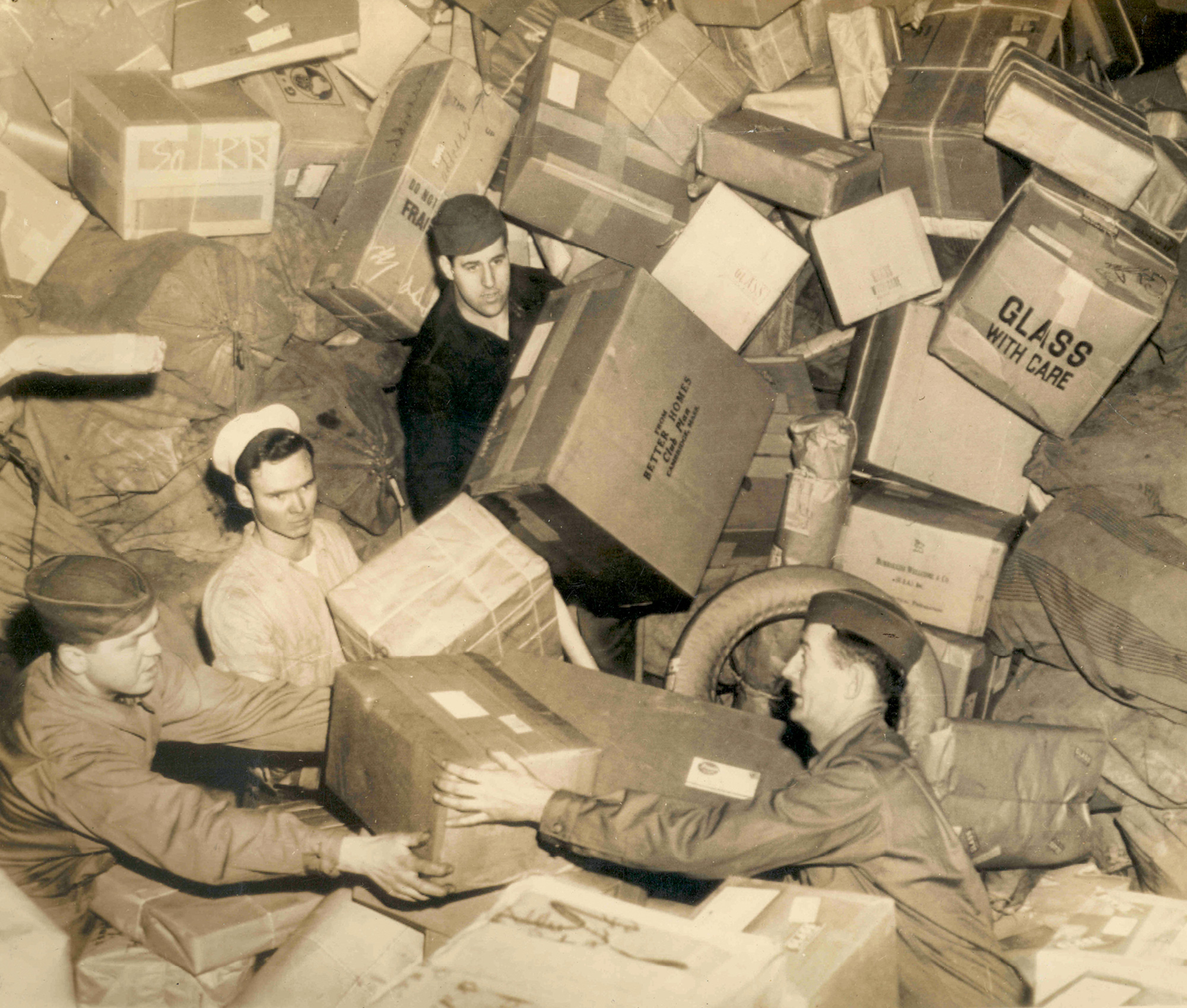 A circa nineteen forty-four photograph of American military personnel amid a mountain of holiday packages.