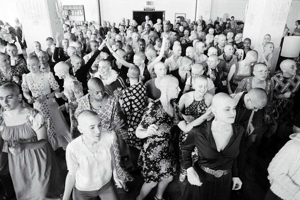A photograph of female Synanon members with shaved heads dancing at an Oakland, California, press conference in nineteen seventy-five. Shaved heads became de rigueur after Dederich adopted the style.