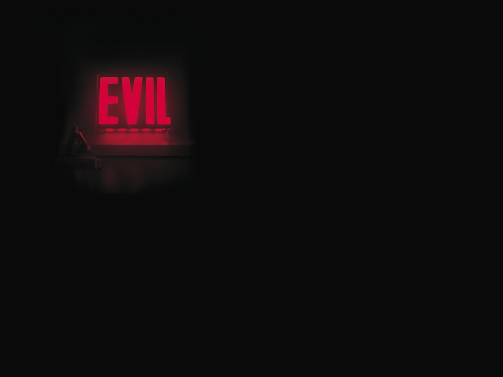 A photograph of artist Vincent Mazeau's Evil/Exit sign lit up in red in a room with all other lights turned off.