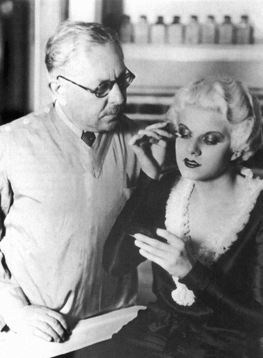 A nineteen thirty-one publicity photograph of Max Factor watching as Jean Harlow applies his company’s mascara.