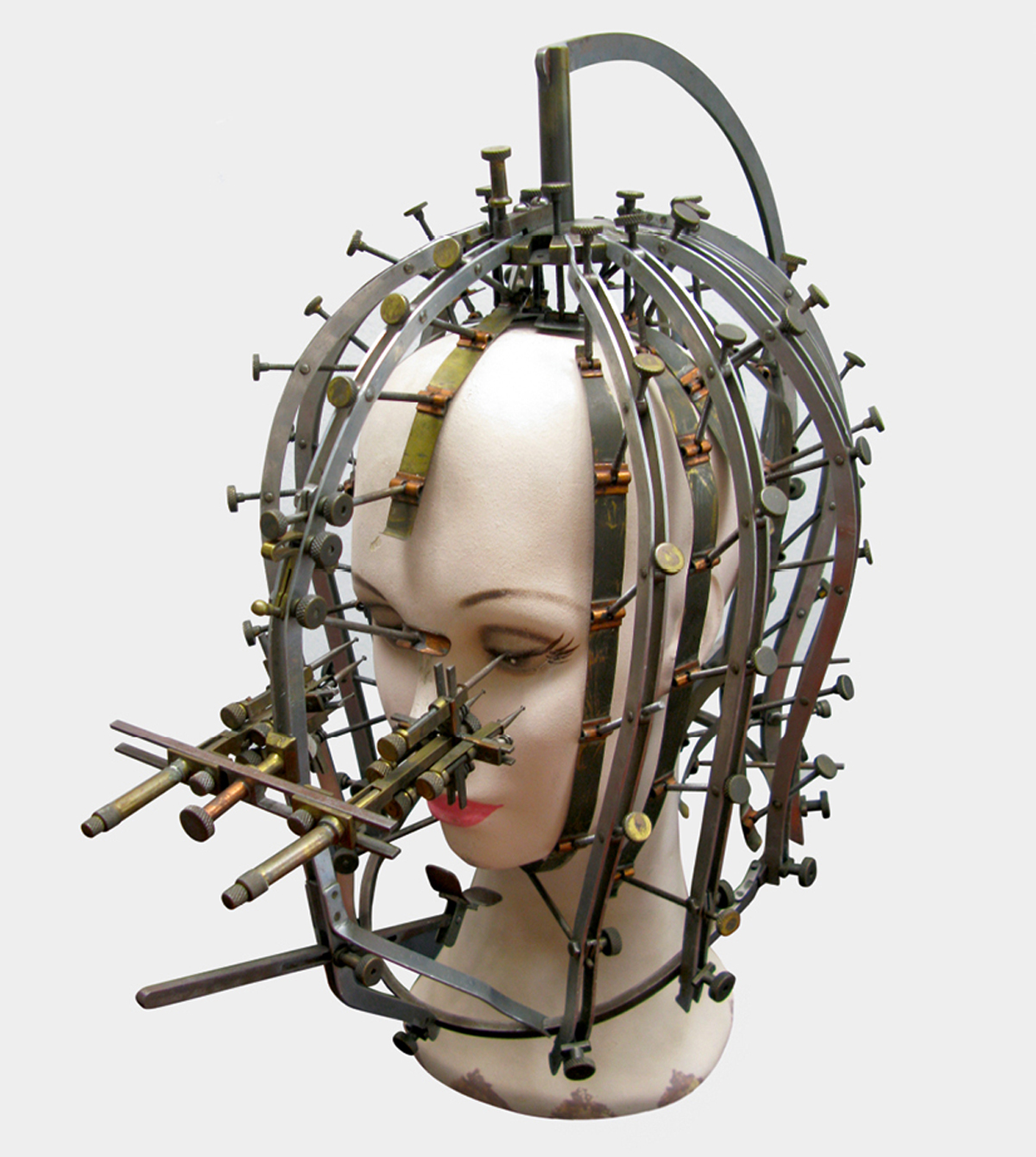 An image of a contraption on a model head called the “Beauty Calibrator,” invented by Factor in nineteen thirty-two. The device, which measured the degree to which a person’s face and head differed from what was deemed to be ideal, was used to determine the most effective makeup solution.