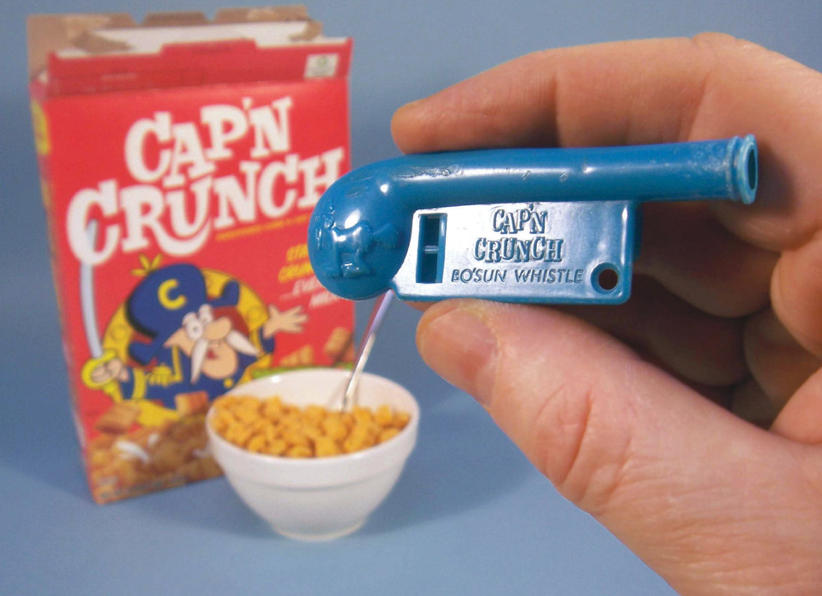 A postcard depicting a photograph of a Cap’n Crunch plastic toy whistle, and a bowl of the cereal next to a Cap’n Crunch box.