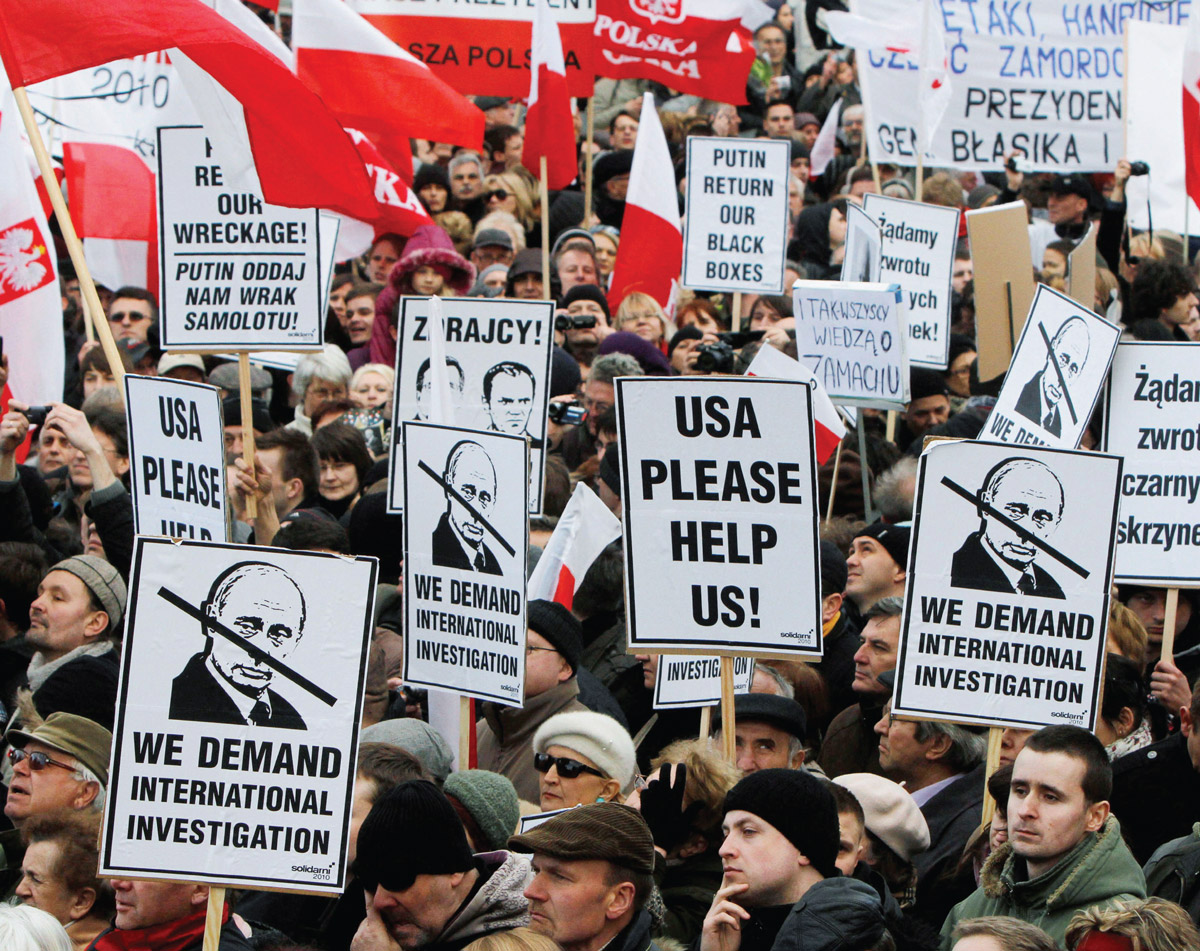 A photograph of a demonstration in Warsaw on April tenth two thousand and eleven marking the first anniversary of the plane crash in Smolensk, Russia. Signs read “we demand internal investigation” and “USA please help us.”