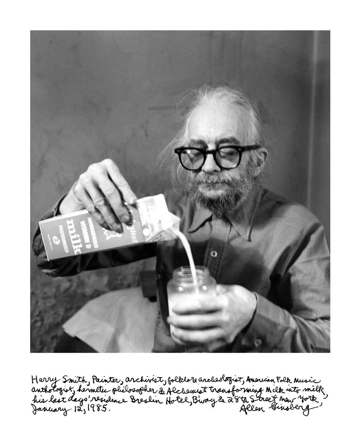 The front of a postcard, featuring Allen Ginsberg’s nineteen eighty five photograph captioned “Harry Smith Transforming Milk into Milk,” of Harry Smith pouring milk into a half-full glass of milk, with a handwritten scrawled caption that reads, “Harry Smith, painter, archivist, folklore archeologist, American folk music anthologist, hermetic philosopher and alchemist transforming milk into milk, his last day o’ residence Breslin Hotel, B’way and Twenty Eighth Stress New York, January Twelfth Nineteen Eighty Five, Allen Ginsberg.”
