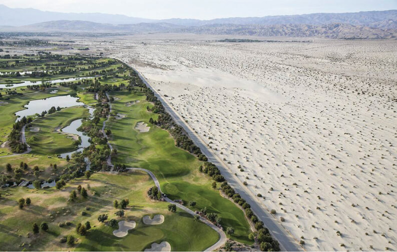 A photograph of a groomed golf course in Palm Springs separated by a highway road from an expansive drought-ridden desert.