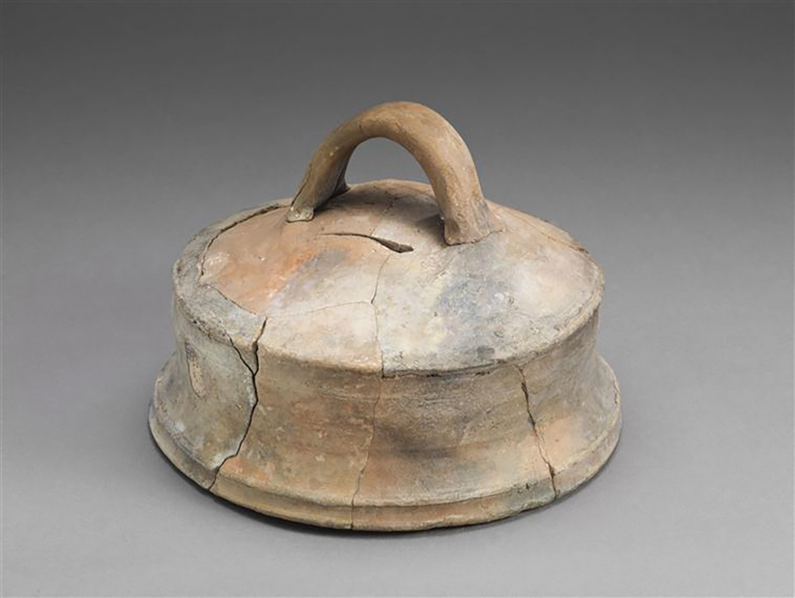 A photograph of an undated couvre-feu, a dome-shaped earthen lid. This couvre-feu is cracked.