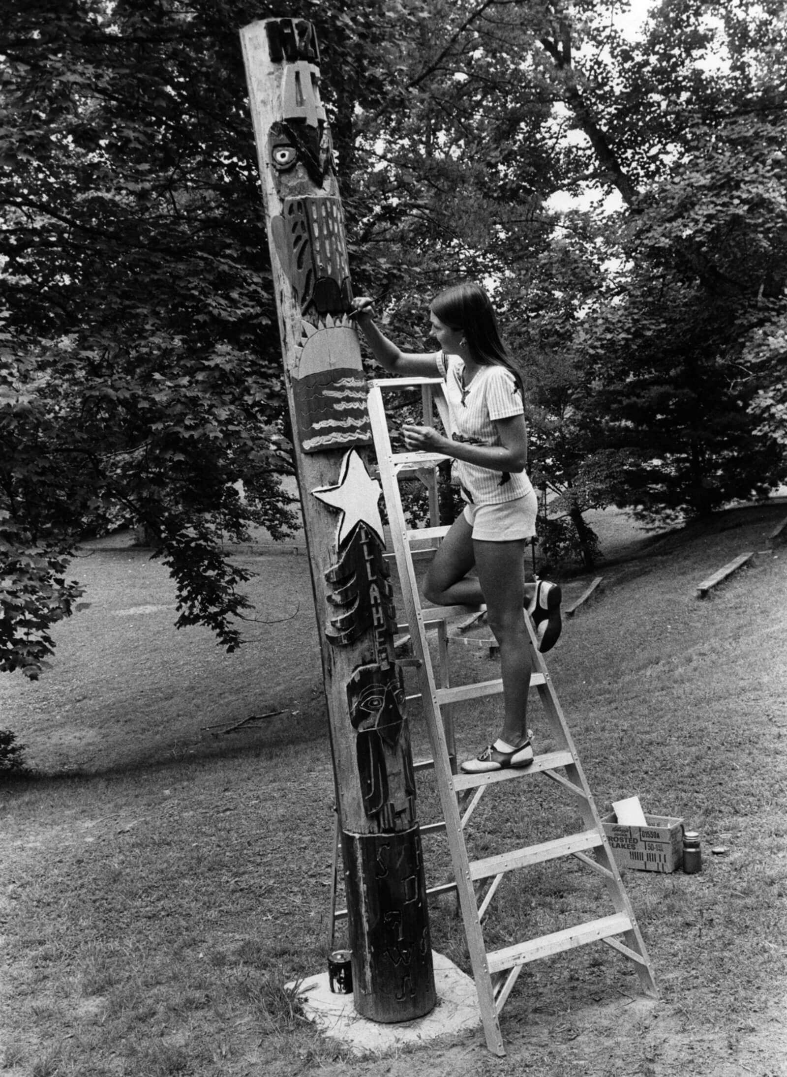 A nineteen seventies photograph of a girl decorating a supposed “totem pole” at Camp Illahee, North Carolina.