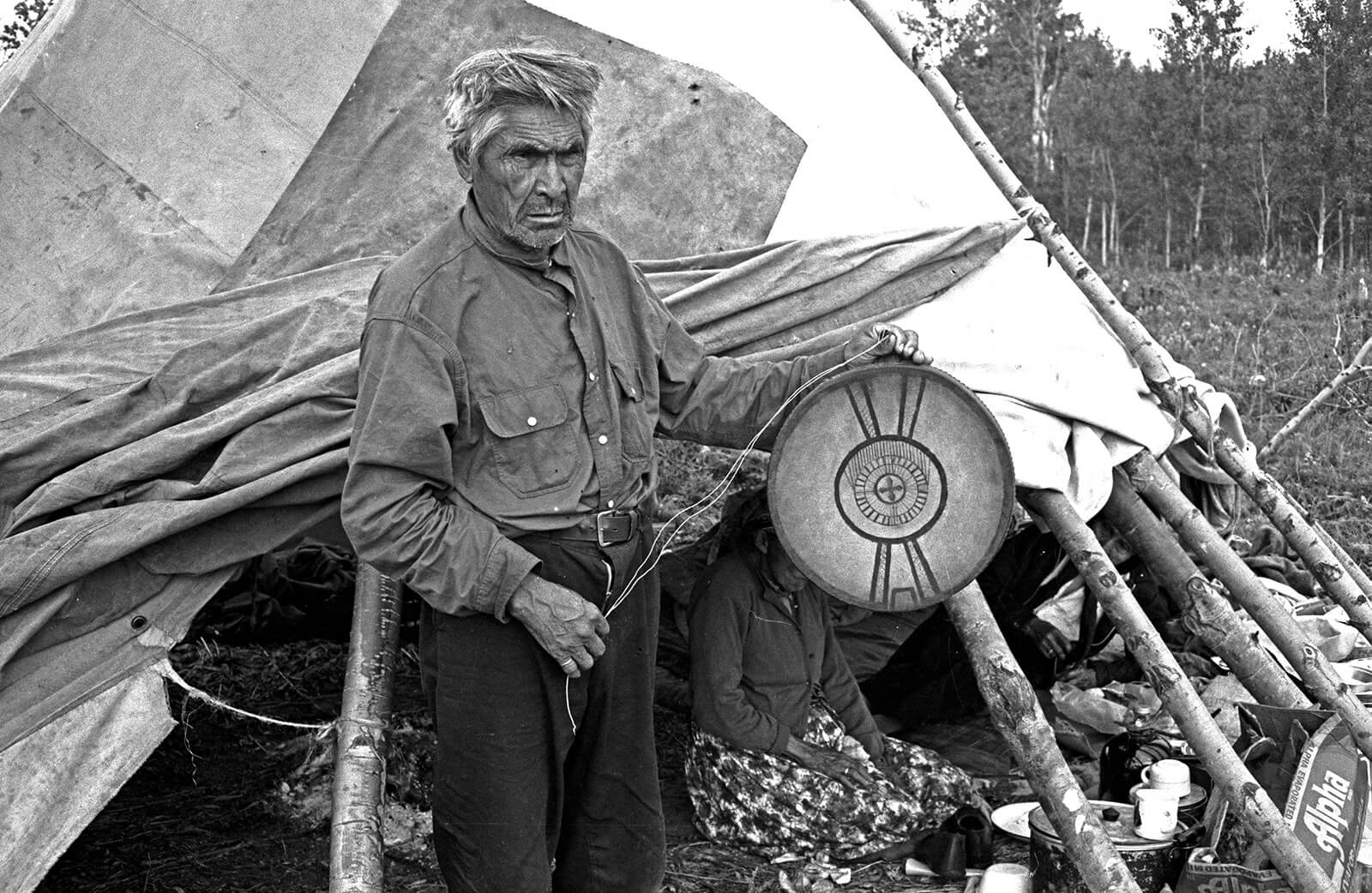 A photograph of Dane-zaa Dreamer Charlie Yahey, carrying a drum emblazoned with a map of the Dane-zaa cosmos.