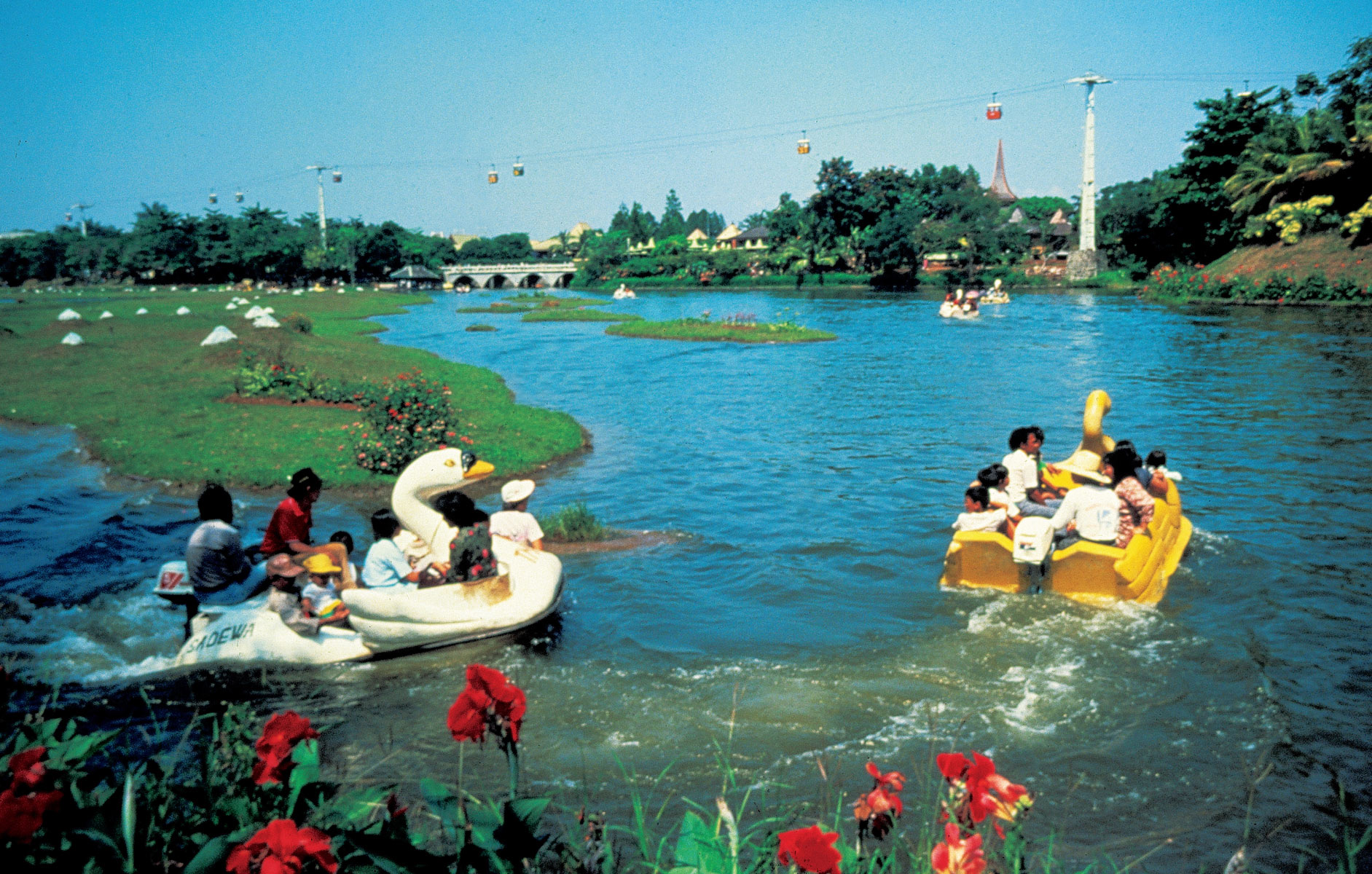 A photograph of park visitors riding in swan-shaped motorboats at Taman Mini.