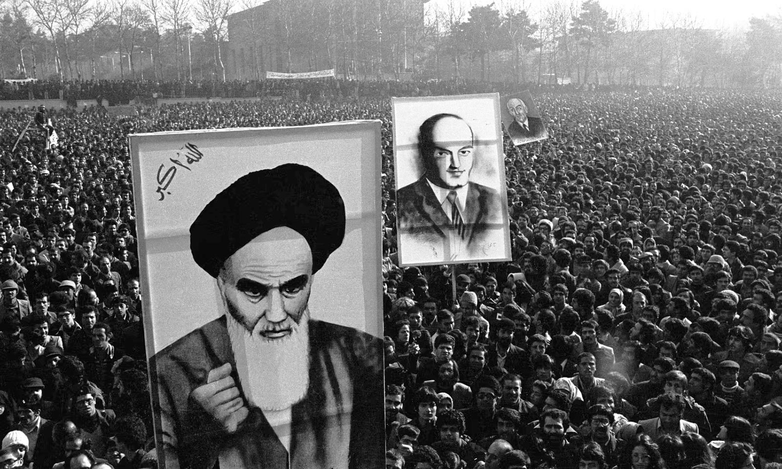 A photograph taken on thirteen January nineteen seventy-nine of a large demonstration on the University of Tehran campus. The crowd holds up three placards depicting Ayatollah Khomeini, Ali Shariati, and Mohammad Mosaddegh, the leader of the oil nationalization movement.