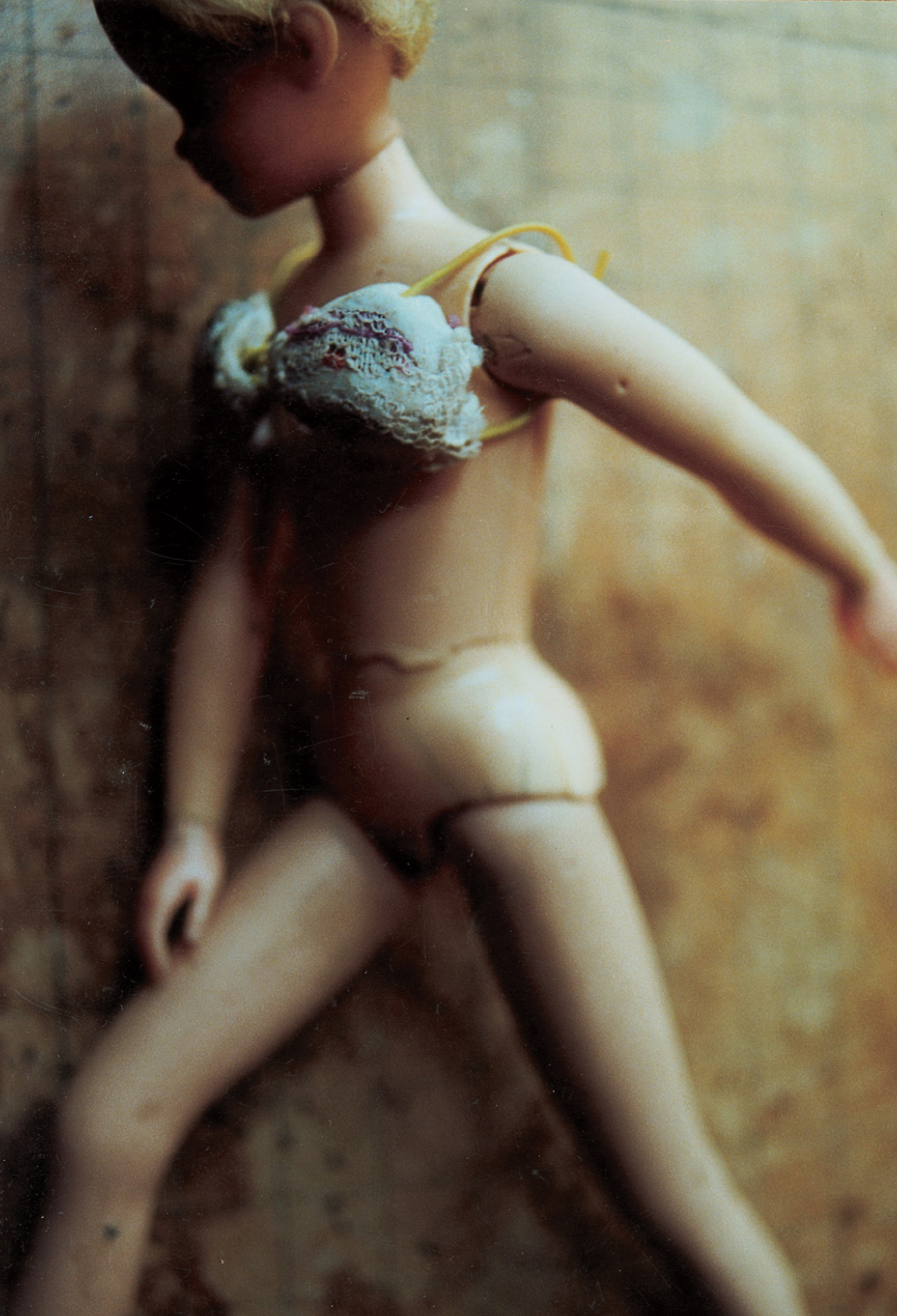A photograph depicting a female doll named Aina. The caption reads: Presented to S. Jackson under the name “Fluff” in Christmas of 1970 or 1971, Aina became the Doll Games’ first and finest heroine. A cheeky tomboy with cropped hair and a wide smile, Aina led the games through most of their finest years together with Laurie, her sidekick and romantic partner, playing such roles as runaway princess, orphan girl, and pirate apprentice with pluck and panache. Aina acquired a second head some years after the first, and alternated between the two thereafter. She was supplanted by identical twins Mara and Melanie in the later Doll Games; this is generally considered to mark the beginning of the decadent era, and of the Doll Games’ eventual decline.